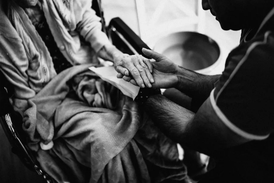 Mani di un caregiver che tengono quelle di una persona anziana in carrozzina