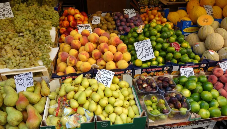Banco di frutta con uva, pesche, pere, agrumi e meloni in un mercato italiano