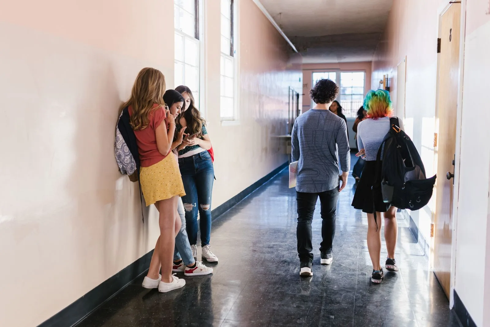 Studenti in un corridoio scolastico con smartphone e zaini