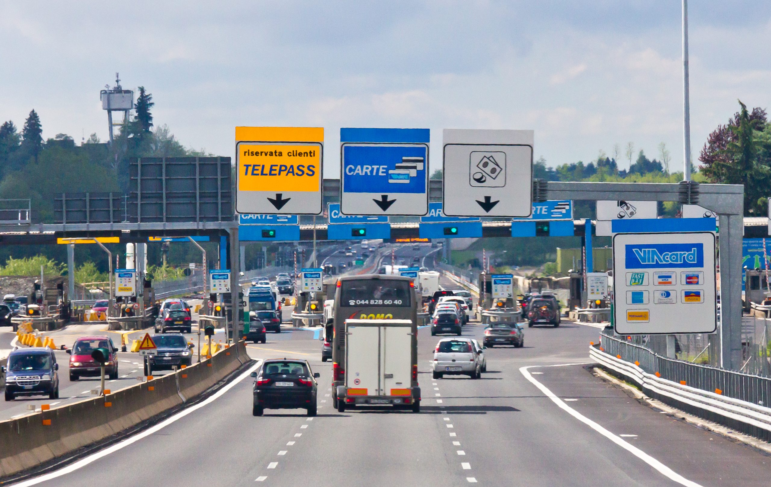 Casello autostradale italiano con auto in transito e corsie Telepass e carte