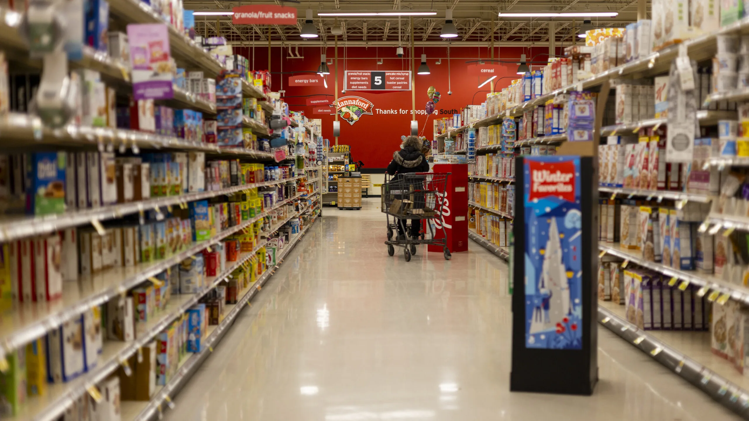 Corsia di supermercato con scaffali pieni e un carrello della spesa