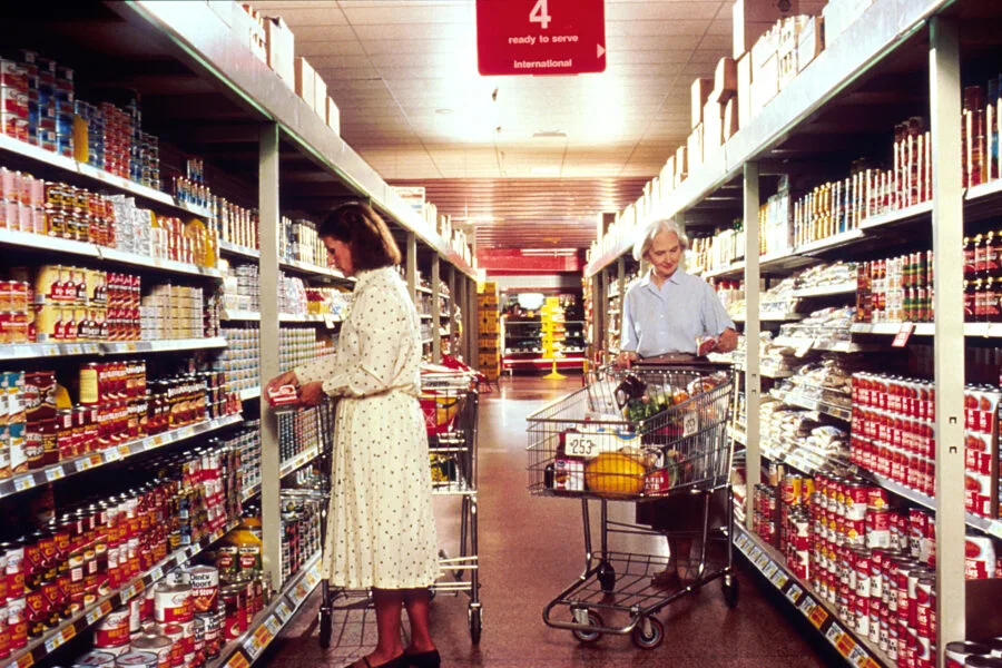 Due persone fanno la spesa tra gli scaffali di un supermercato