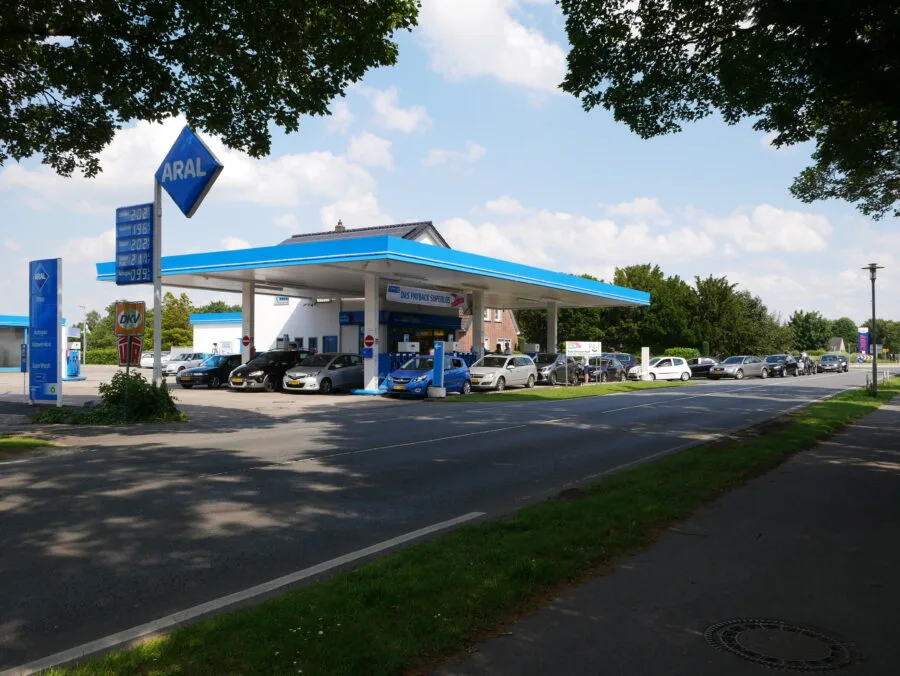 Stazione di servizio europea con auto in coda e tabellone prezzi carburanti