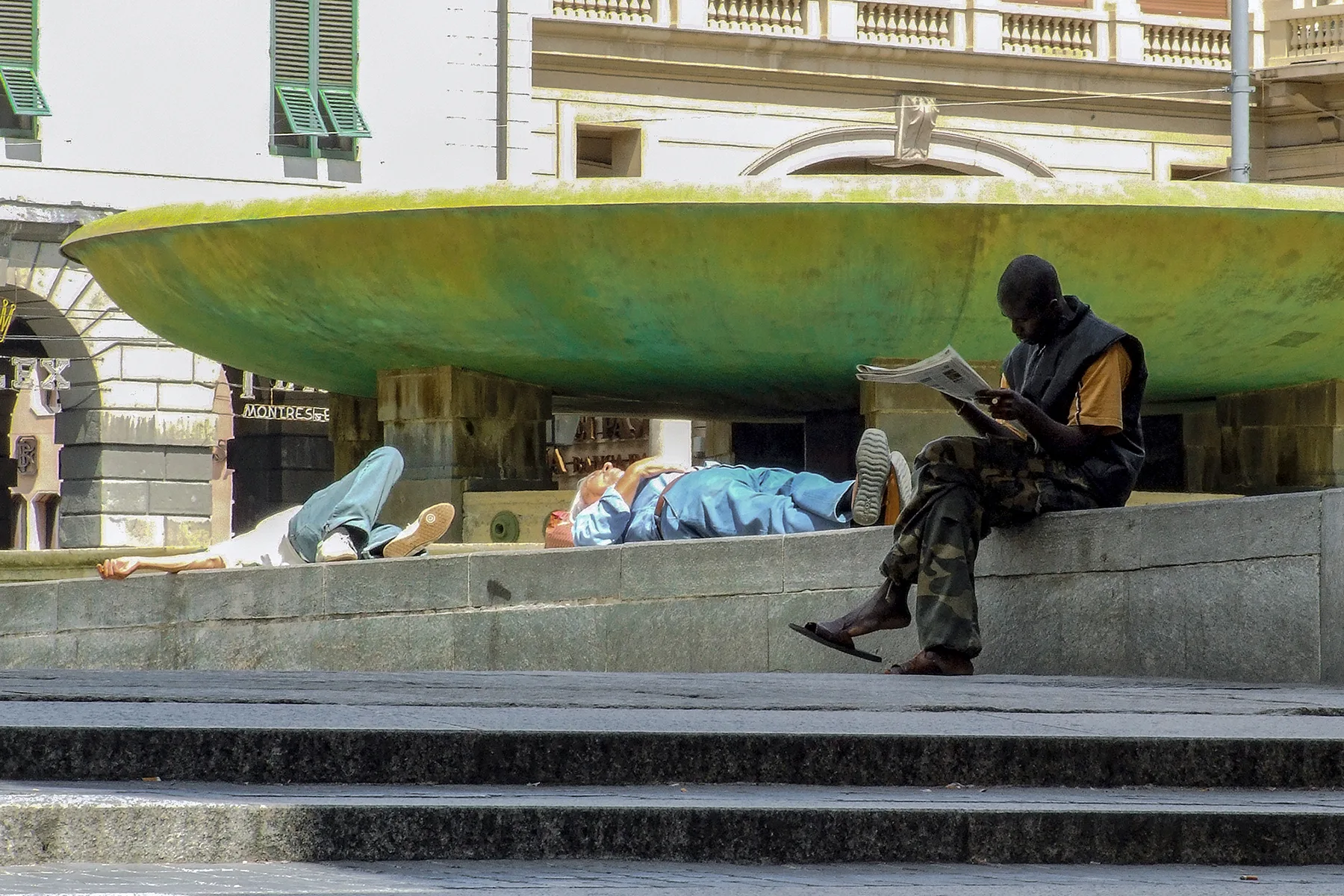 Persone riposano all ombra della fontana di Piazza De Ferrari a Genova durante una giornata estiva calda