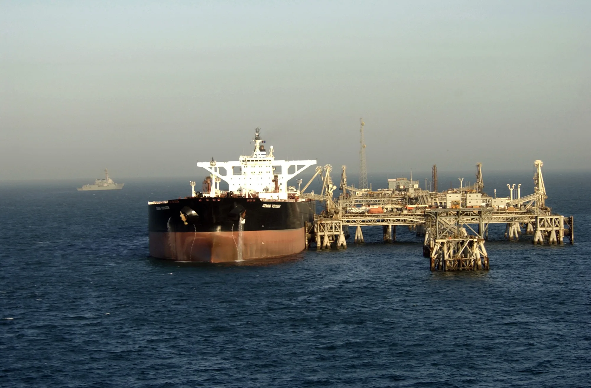 Petroliera in un terminal petrolifero nel Golfo Persico con nave militare sullo sfondo