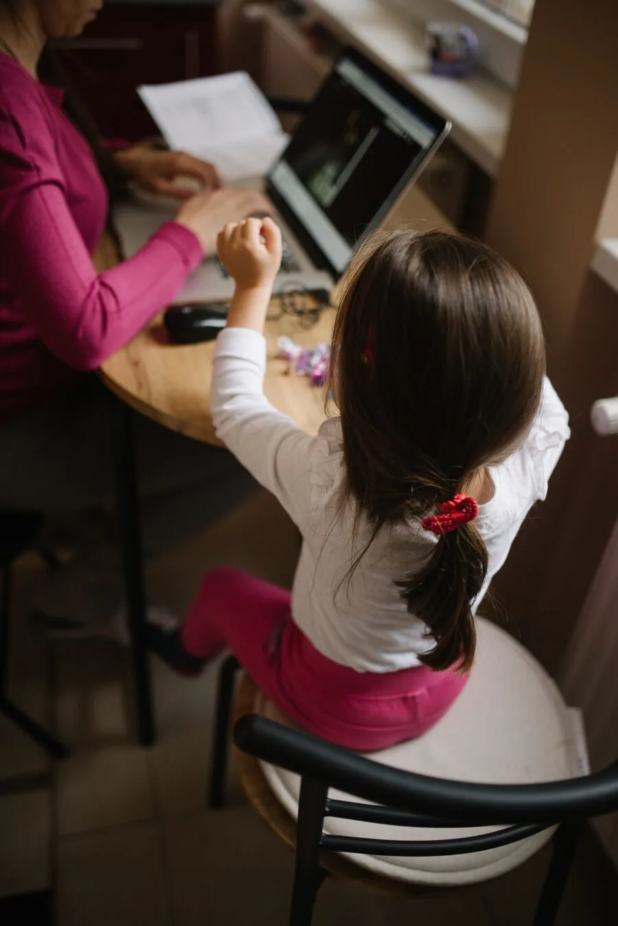 Una bambina gioca accanto al genitore che scrive al computer da casa