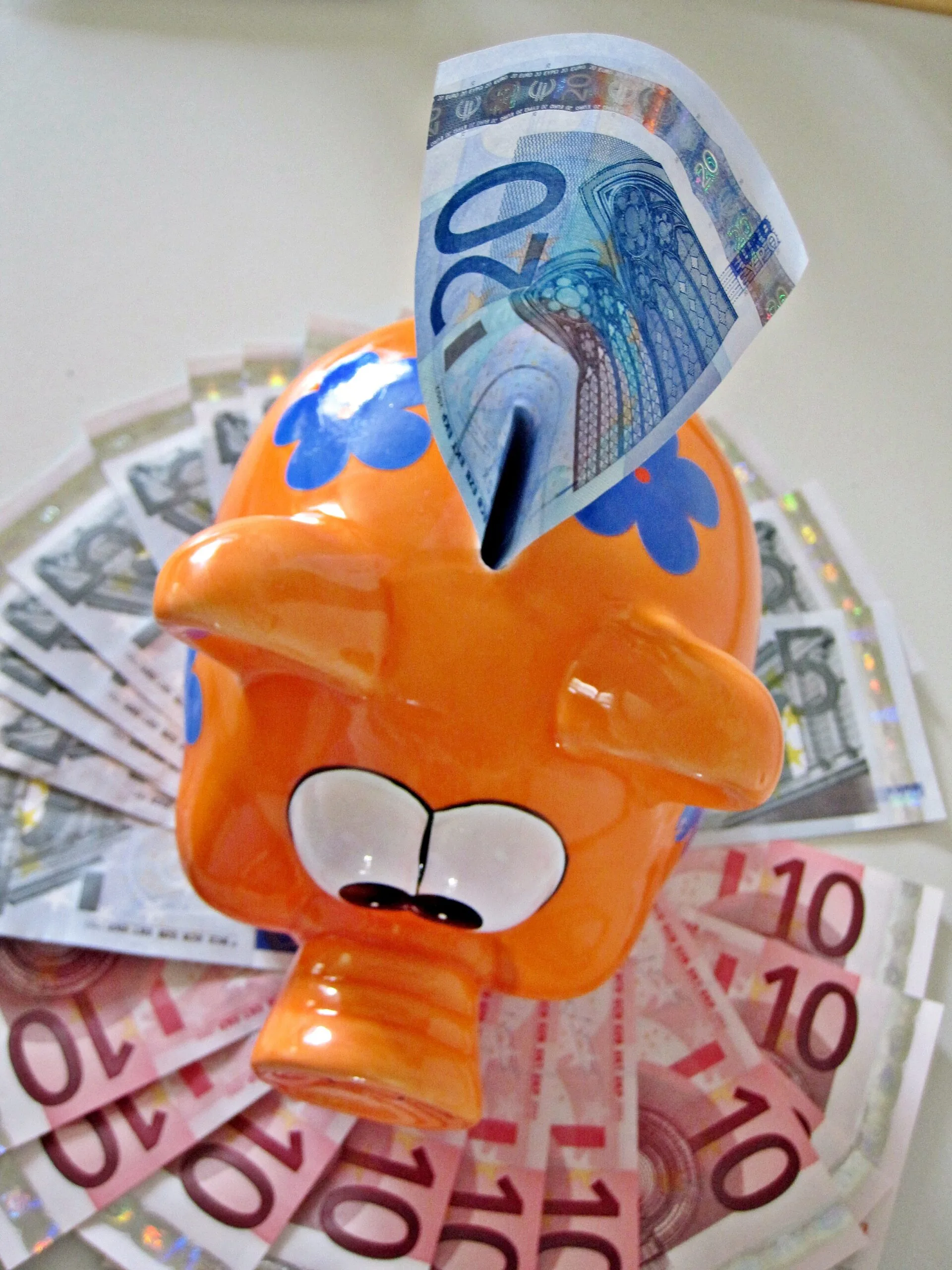 Salvadanaio arancione con una banconota da 20 euro e altre banconote, foto d’archivio