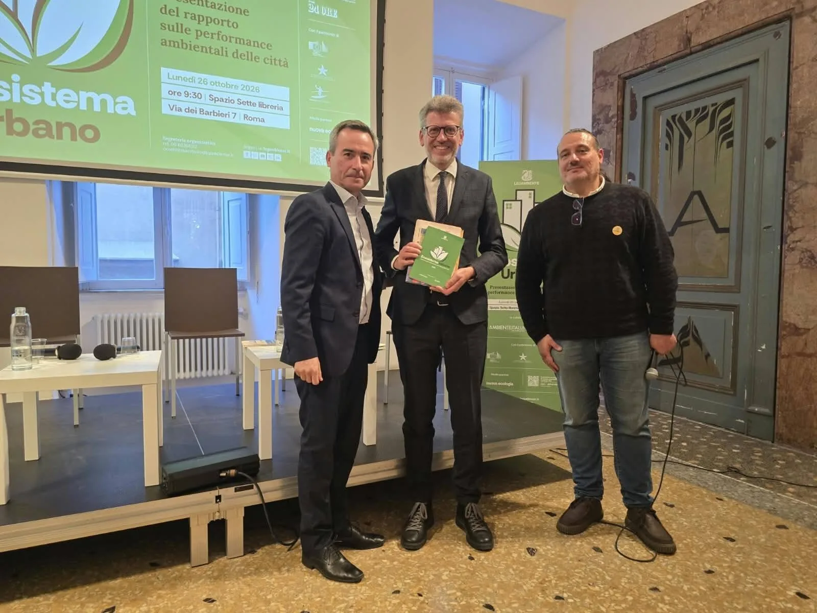 Tre partecipanti con il riconoscimento di Ecosistema Urbano 2026 davanti allo schermo della presentazione