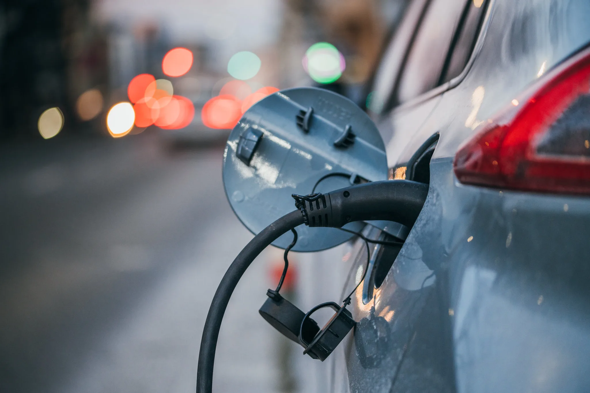 Cavo collegato alla presa di ricarica di un’auto elettrica, con luci del traffico sullo sfondo