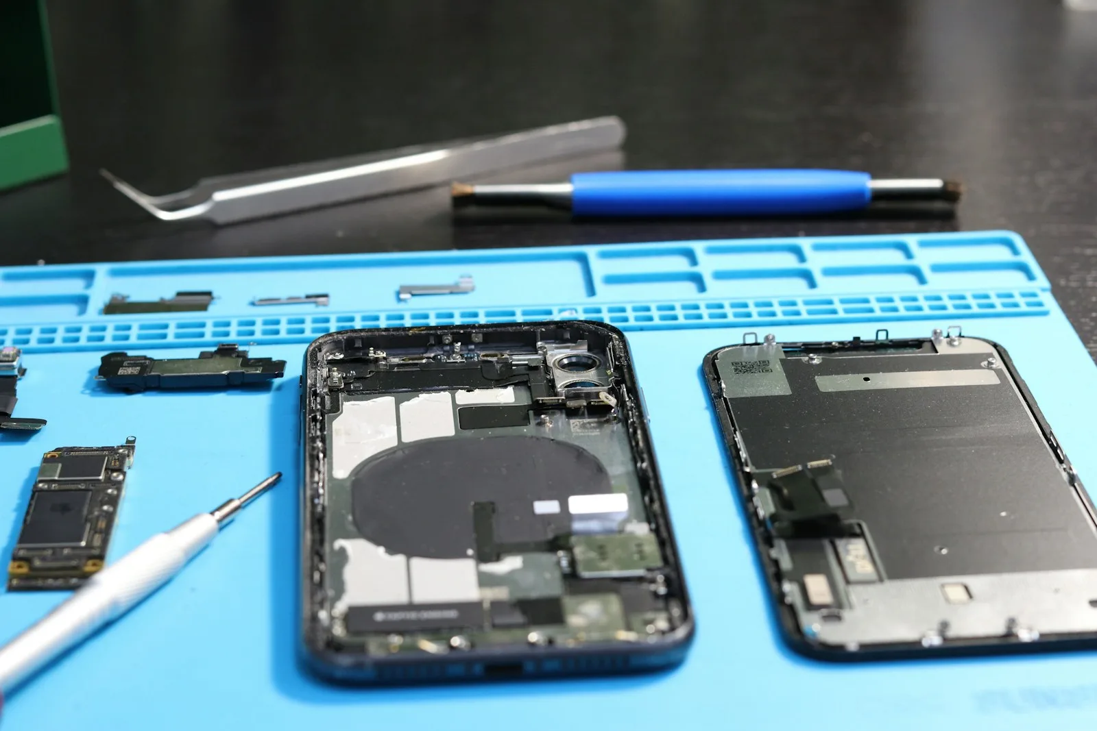 iPhone tradizionale smontato su un tappetino azzurro con utensili di riparazione