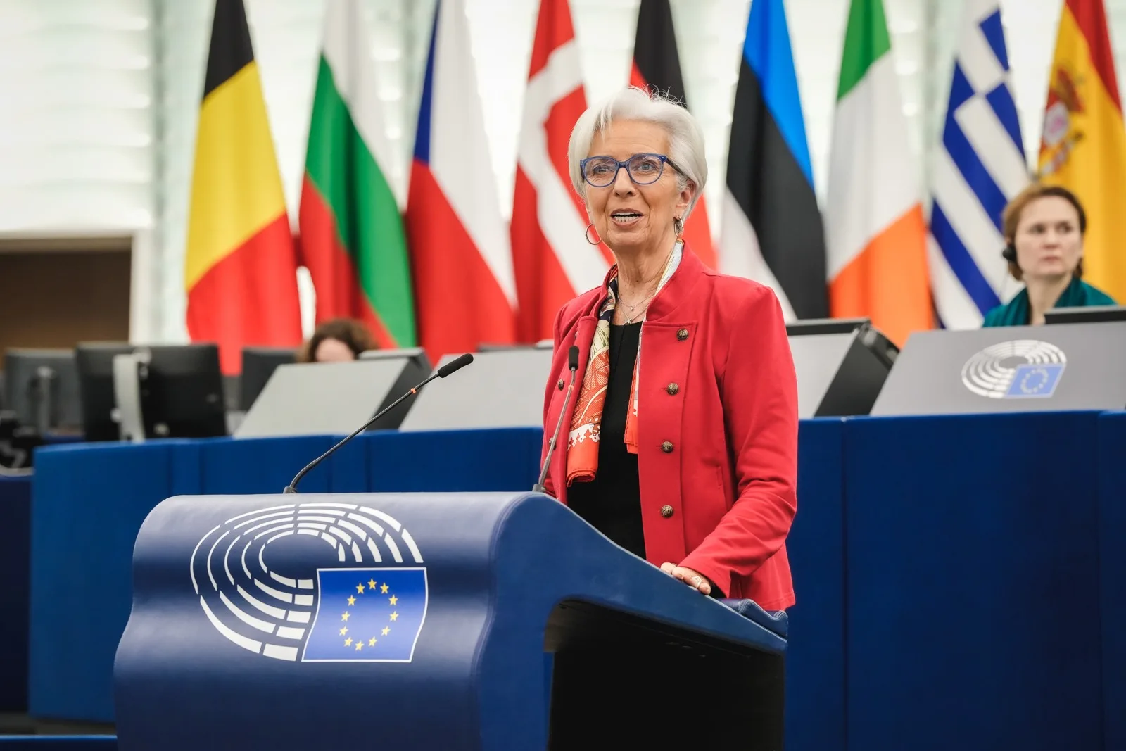 Christine Lagarde parla a un podio del Parlamento europeo davanti alle bandiere nazionali