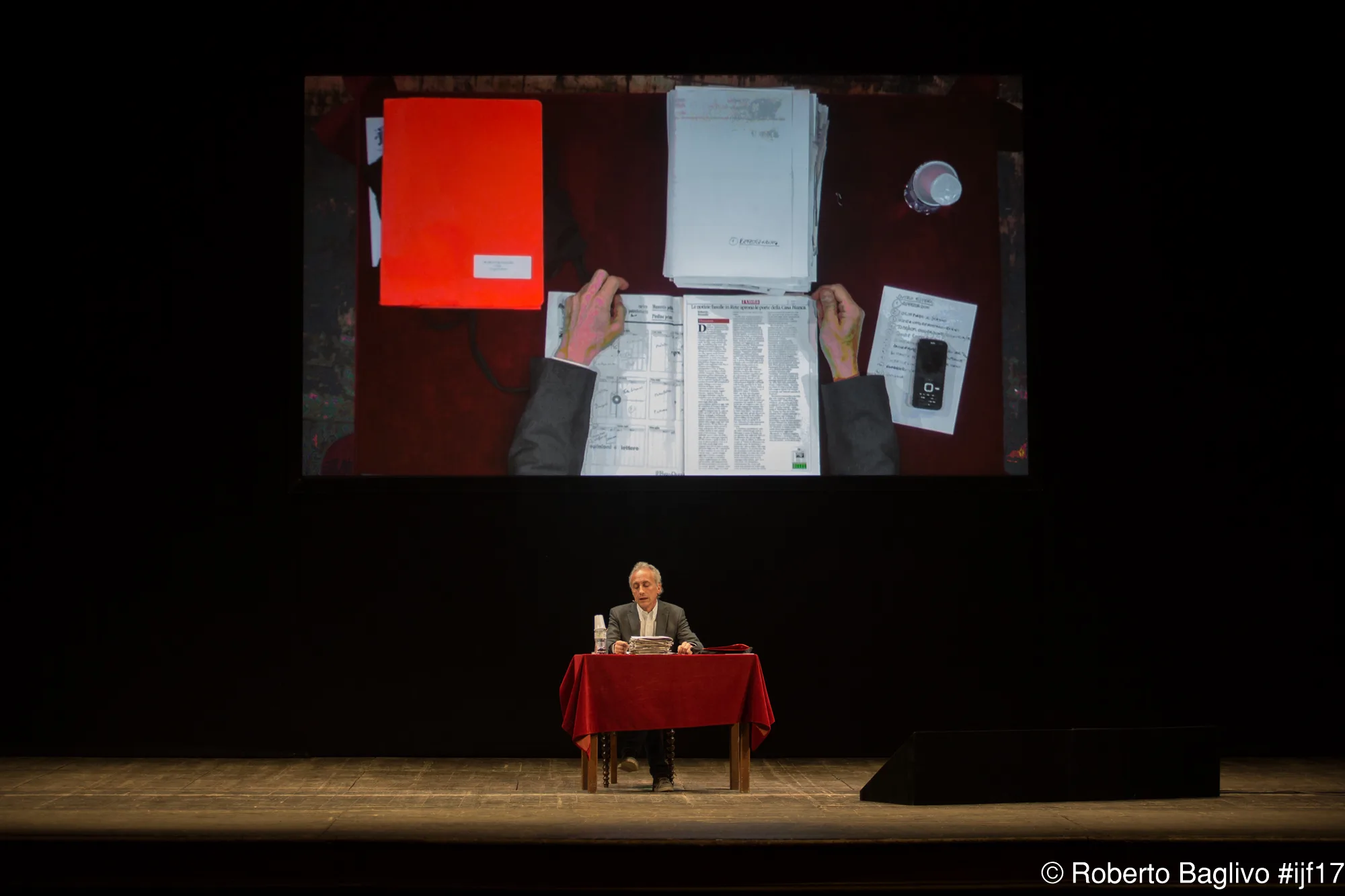 Marco Travaglio seduto a un tavolo sul palco del Festival del giornalismo nel 2017