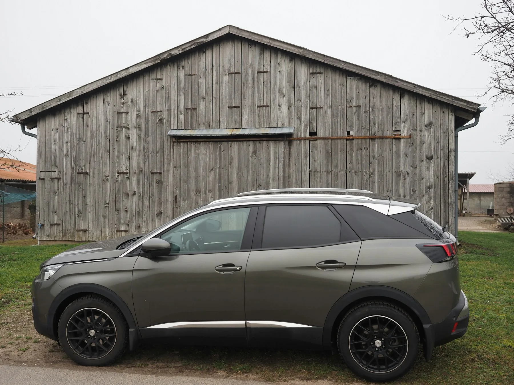 Peugeot 3008 grigia vista di lato davanti a un edificio in legno