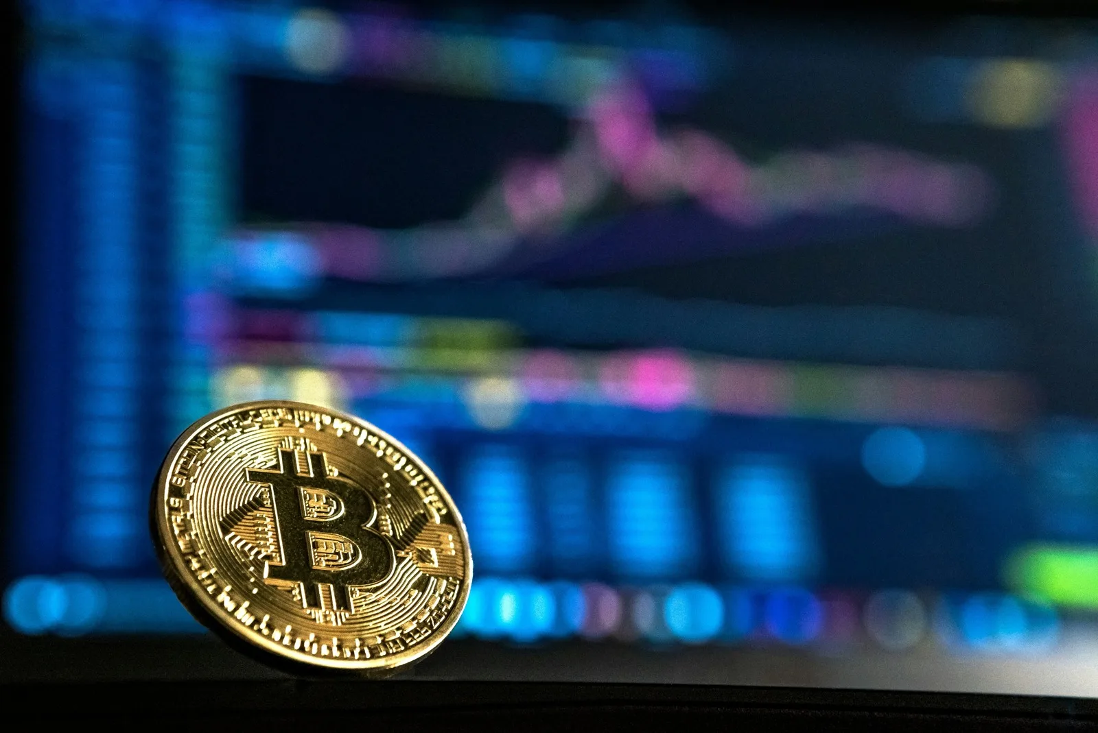 Gettone dorato con il simbolo Bitcoin davanti a uno schermo sfocato