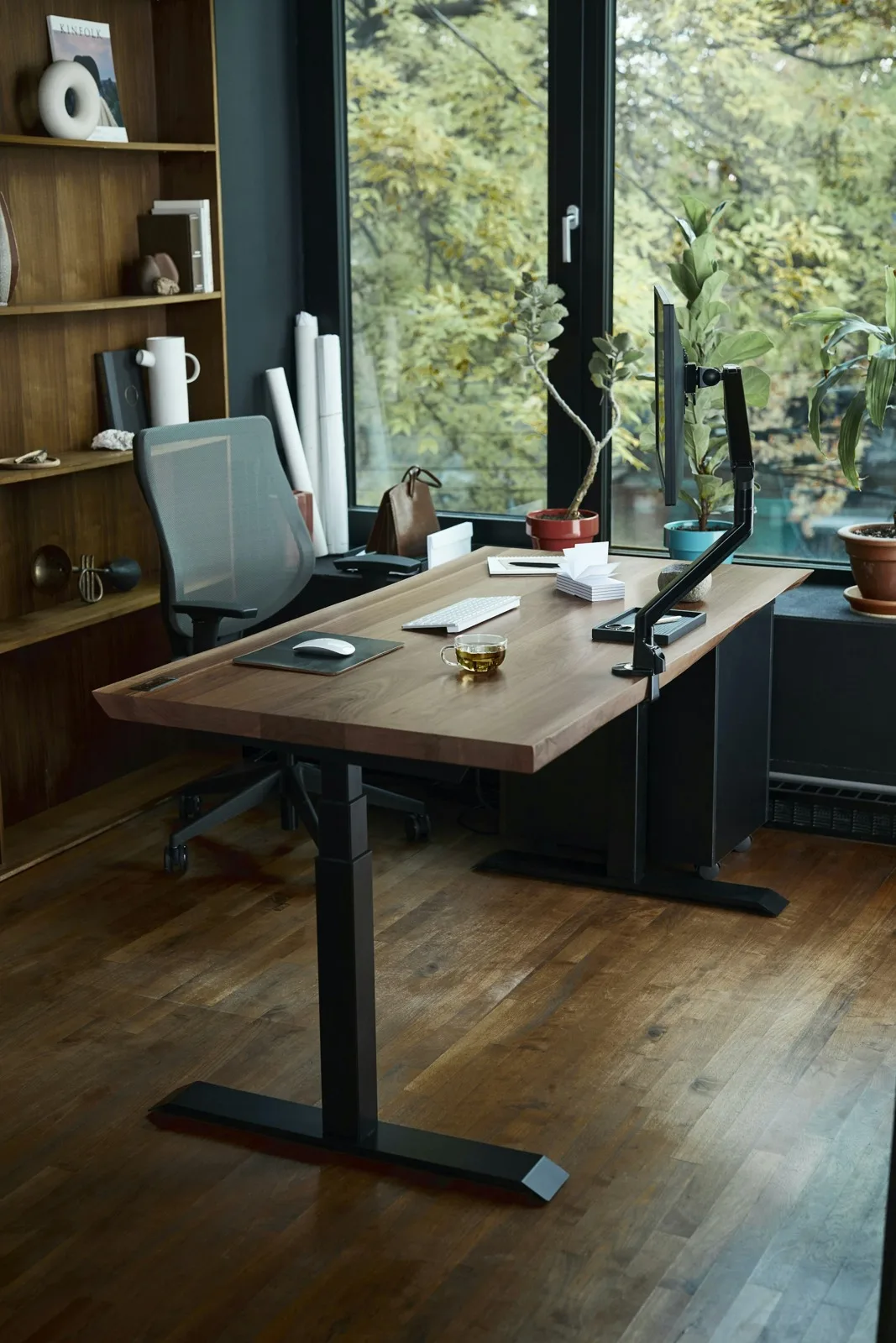 Scrivania in legno con monitor, tastiera e sedia accanto a una finestra