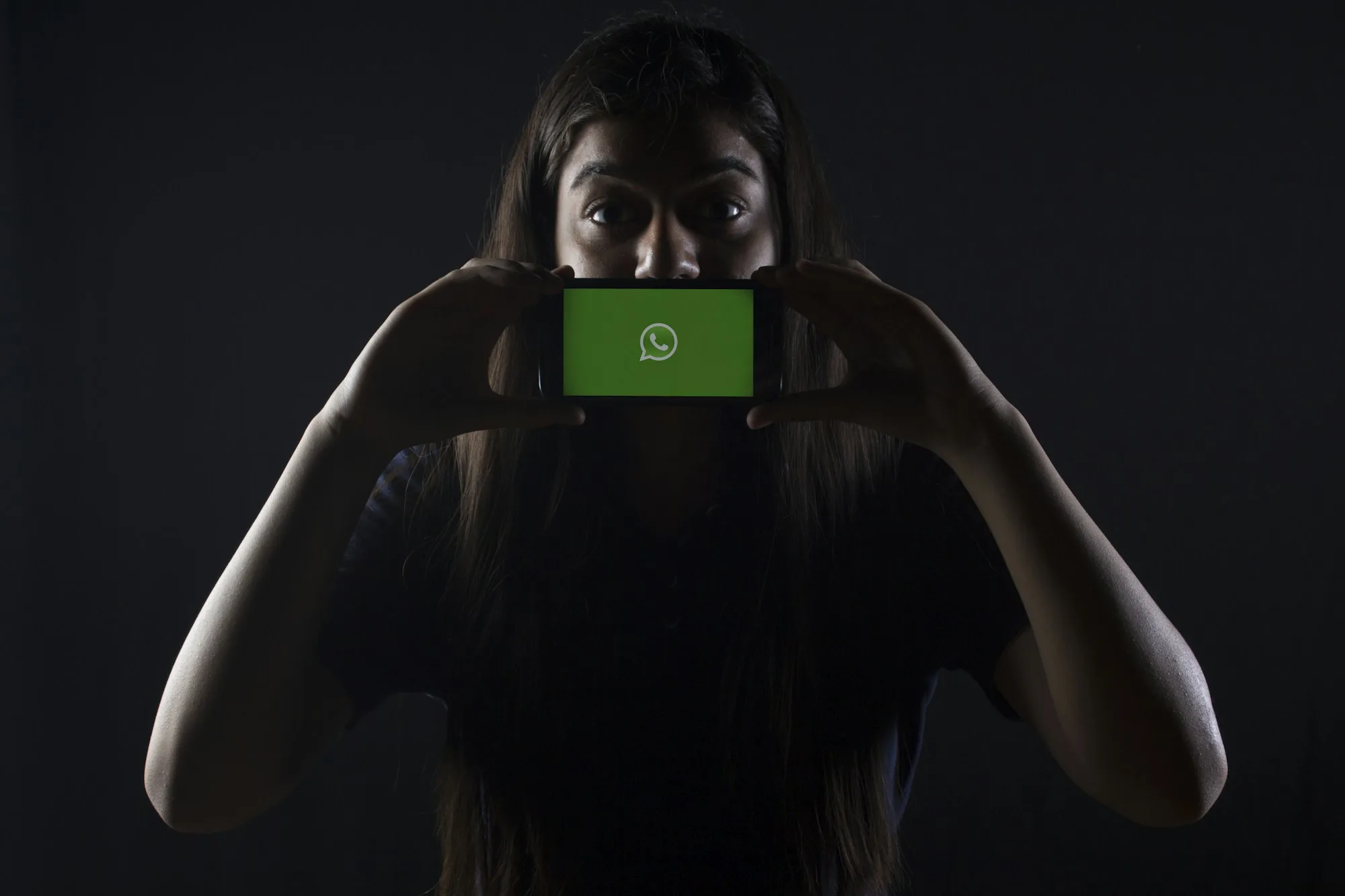 Una donna tiene un telefono in orizzontale con il logo WhatsApp sullo schermo